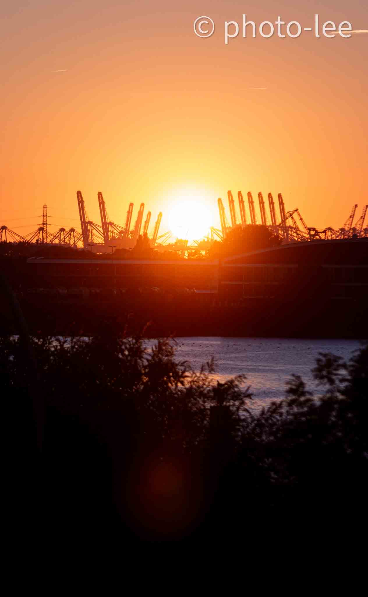Die Sonne geht zwischen den Kränen des Hamburger Hafens unter